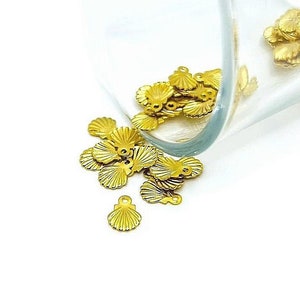 May include: A glass jar filled with gold-colored metal seashell charms. The charms are spilling out of the jar onto a white surface.