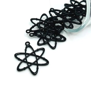 May include: A pile of black metal atom charm pendants, spilling out of a glass jar. The charms are in the shape of an atom with a circle in the center and five points.