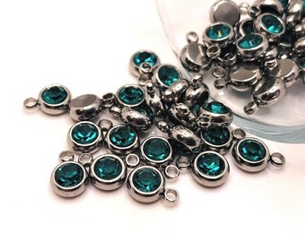 May include: A pile of teal blue crystal charms with silver metal loops. The charms are scattered on a white surface.