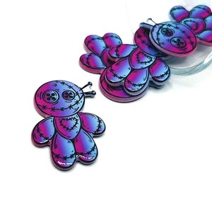 Può includere: Un gruppo di piccoli ciondoli a forma di bambola voodoo colorati con un effetto sfumato rosa e blu. Le bambole hanno dettagli cuciti e occhi a bottone.