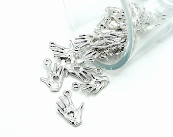 Puede incluir: Un tarro de vidrio lleno de colgantes de plata con forma de manos con un corazón en la palma. Los colgantes se derraman del tarro sobre una superficie blanca.