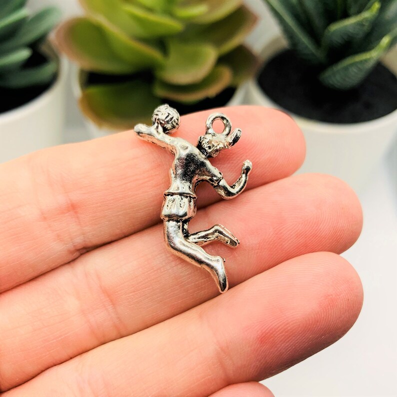 May include: Silver charm of a volleyball player spiking the ball. The charm is detailed and has a realistic design.
