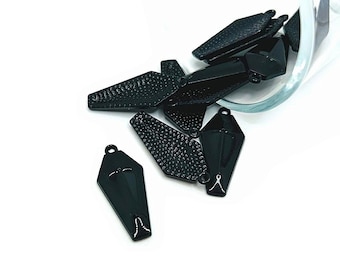 May include: A group of black metal charms in the shape of a coffin and a diamond. The charms have a textured surface and are scattered on a white background.
