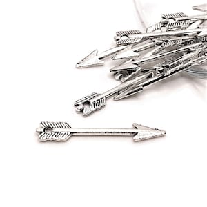 May include: A pile of silver arrow charms with a single arrow charm laying on its side. The arrow charms have a simple design with a pointed tip and a fletched tail.