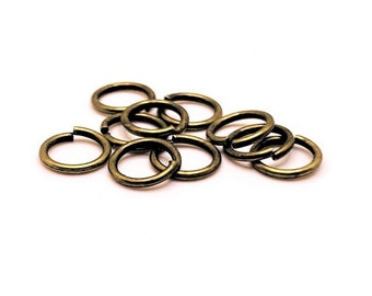 Könnte beinhalten: Eine Gruppe von 10 goldenen Sprungringen, eine Art von Schmuckzubehör, liegt auf einer weißen Oberfläche verstreut. Die Ringe sind klein und rund, mit einer glatten, polierten Oberfläche.