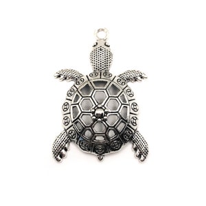 Könnte beinhalten: Silberfarbener Metallschildkrötenanhänger mit einem detaillierten, durchbrochenen Muscheldesign. Der Anhänger hat eine Öse oben zum Anbringen an Schmuck oder anderen Bastelarbeiten.