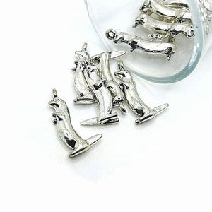 May include: Silver charm pendants shaped like dachshunds. The charms are scattered on a white surface and in a clear glass jar.
