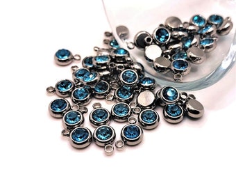 May include: A large group of blue crystal beads with silver loops. The beads are scattered on a white surface.
