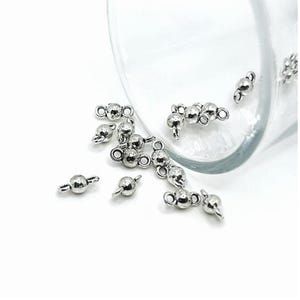 May include: Silver-toned metal bead connectors with two loops on each side. The beads are round and have a textured surface.