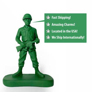 May include: A green plastic toy soldier holding a rifle, standing on a green base. The soldier is wearing a green helmet and has a green face. A speech bubble above the soldier says "Fast Shipping! Amazing Charms! Located in the USA! We Ship Internationally!"