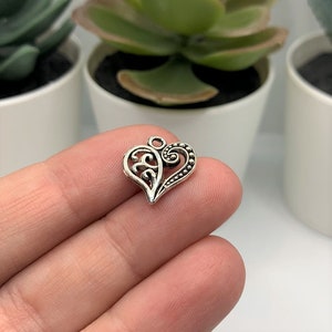 May include: Silver charm in the shape of a heart with a decorative filigree design.