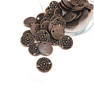 May include: A pile of antique copper-toned metal round charms with a floral design and two holes.