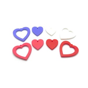 May include: A collection of heart-shaped charms in various colors, including red, pink, purple, and white. Some are solid, while others have a heart-shaped cutout. Each charm has a small hole for stringing.