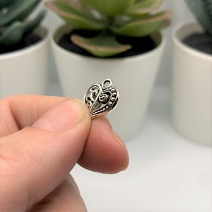 May include: Silver heart charm with an intricate design. The heart has a swirl pattern and is accented with small beads.