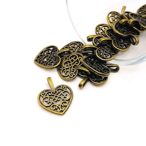 May include: A pile of antique gold filigree heart charms with intricate designs. The charms are scattered on a white surface.