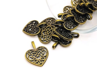 May include: A pile of antique gold filigree heart charms with intricate designs. The charms are scattered on a white surface.