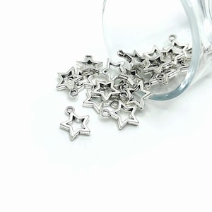 May include: A pile of silver-toned metal star charms with a loop at the top. The charms are scattered on a white surface.
