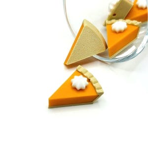 May include: Close-up of several miniature pumpkin pie slices. Each slice features an orange filling, a tan crust, and a dollop of white whipped cream. Some slices are inside a clear glass bowl.