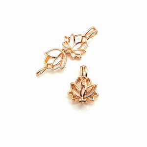 Puede incluir: Dos colgantes de metal en forma de flor de loto de color dorado. Los colgantes están abiertos y se pueden usar para guardar objetos pequeños, como perlas o cristales.
