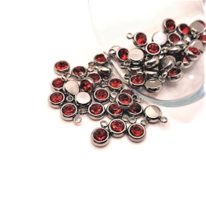 May include: A close-up of a pile of red rhinestone charms with silver loops. The charms are scattered on a white surface.