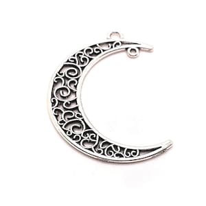 Pode incluir: Encanto de lua crescente em filigrana prateada com um design decorativo. O encanto tem dois laços para prender em joias.