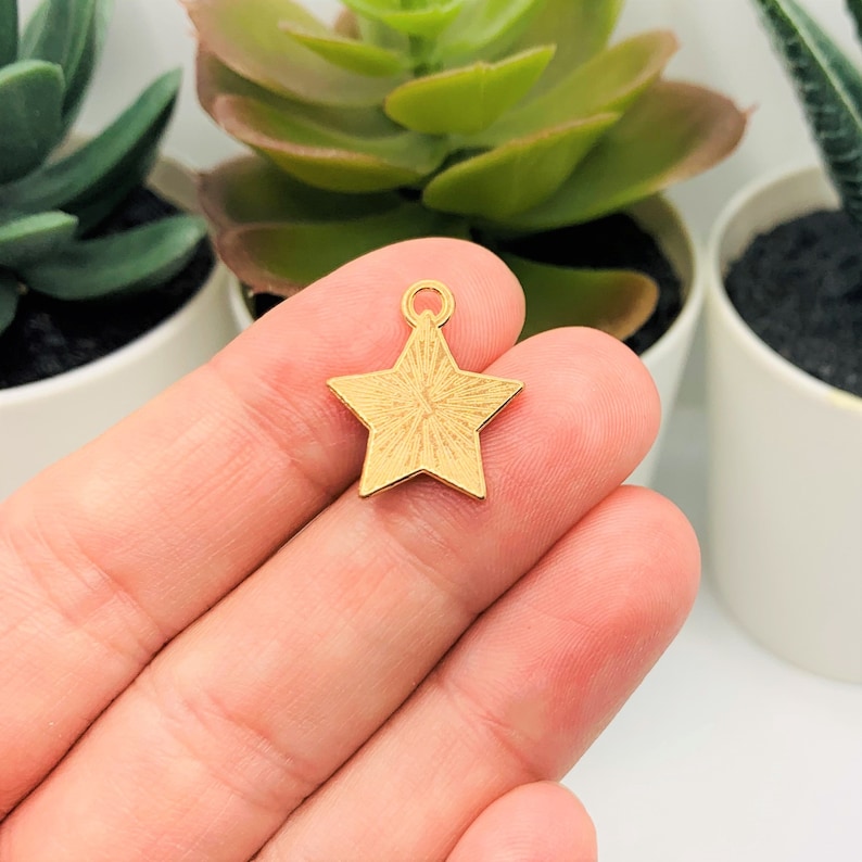 May include: Gold star charm with a textured surface. The charm has a loop at the top for attaching to a necklace or bracelet.