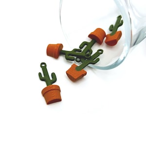 May include: A group of small, green cactus charms with orange pots, spilling out of a clear glass jar. The charms are made of plastic and have a realistic look.