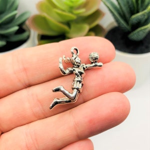 May include: Silver charm of a volleyball player spiking the ball. The charm is detailed and has a realistic design.