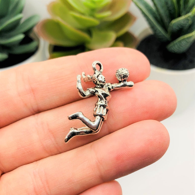 May include: Silver charm of a volleyball player spiking the ball. The charm is detailed and has a realistic design.