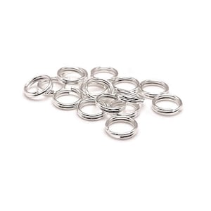May include: A pile of silver jump rings, a type of jewelry finding used for connecting chains, cords, and other jewelry components.