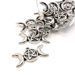 May include: A pile of silver-toned metal charms in the shape of a triple moon with a pentagram in the center. The charms are scattered on a white surface.