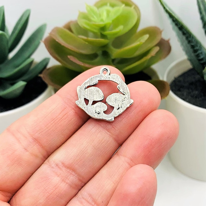 K&ouml;nnte beinhalten: Silberner Anh&auml;nger mit einem ausgeschnittenen Design von zwei Fischen, die sich gegen&uuml;berstehen. Der Anh&auml;nger ist eine beliebte Wahl f&uuml;r die Schmuckherstellung und perfekt, um jedem Projekt einen Hauch von Verspieltheit zu verleihen.