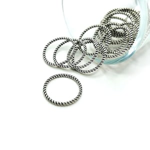 May include: A pile of silver-toned, twisted metal rings in a glass container. The rings are all the same size and have a smooth, polished finish.