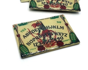 Könnte beinhalten: Ein Ouija-Brett im Vintage-Stil mit der Aufschrift "Black Magic Talking Board". Das Brett ist aus Holz und hat einen gelben Hintergrund mit grünen, roten und schwarzen Akzenten. Das Brett verfügt über eine Planchette, Buchstaben, Zahlen und die Wörter "ja", "nein", "hallo" und "auf Wiedersehen".