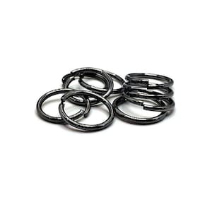 May include: A close-up of a pile of black metal jump rings. The rings are all the same size and are arranged in a random pattern.