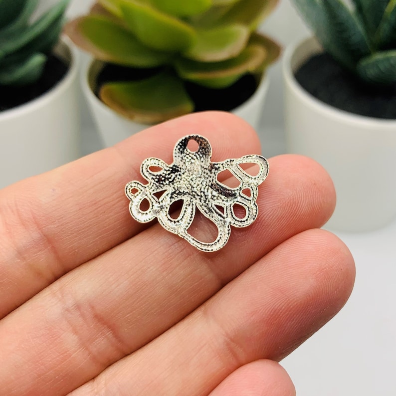May include: Silver metal charm shaped like an octopus with a hole at the top for hanging.