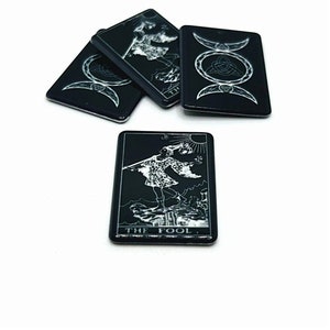 May include: Four black tarot cards with white designs. One card features the Fool card from the Major Arcana. The other three cards feature a triple moon symbol with a Celtic knot.