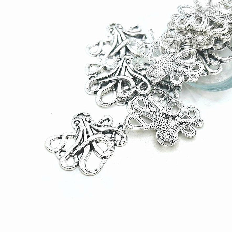 May include: Silver metal octopus charms with intricate details. The charms are scattered on a white surface.