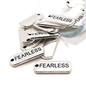 May include: A pile of silver metal tags with the word "Fearless" engraved on them. The tags have two holes for attaching to a necklace or bracelet.