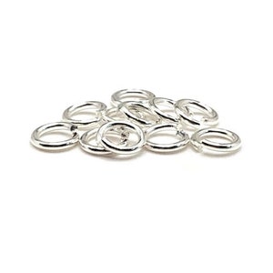 May include: A pile of silver jump rings, a type of jewelry finding used for connecting chains, cords, and other jewelry components.