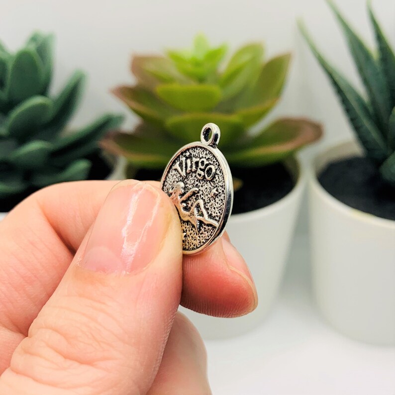 Op de afbeelding: Zilveren bedel met het astrologische teken Maagd en het woord "Maagd" erop gegraveerd.