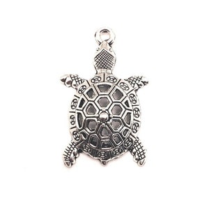 May include: Silver-toned metal turtle charm with a detailed, openwork shell design. The charm has a loop at the top for attaching to jewelry or other crafts.