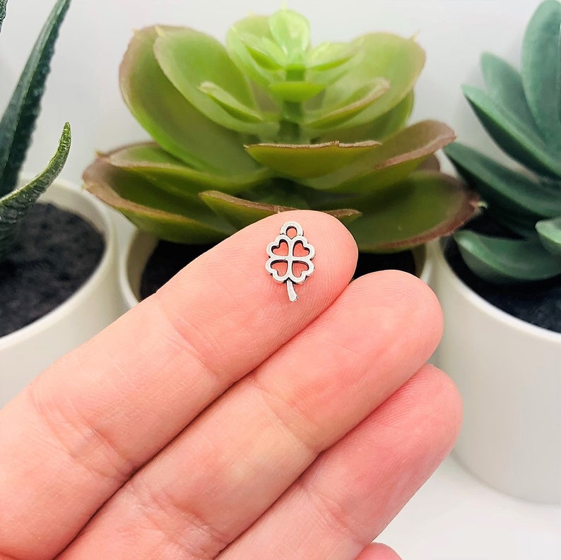 May include: Silver charm in the shape of a four-leaf clover. The charm is small and delicate, perfect for adding a touch of luck to jewelry or crafts.
