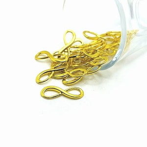 May include: A pile of gold-colored infinity symbol charms, spilling out of a clear glass container.