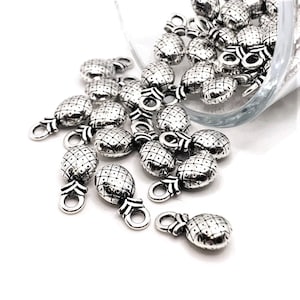 May include: A pile of silver pineapple charm pendants with a textured surface. The charms have a small loop at the top for attaching to jewelry or other crafts.