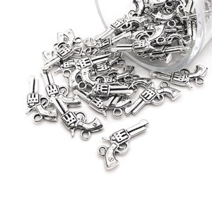 May include: A large quantity of silver-toned metal gun charms, scattered on a white surface. The charms are detailed with a realistic gun design.