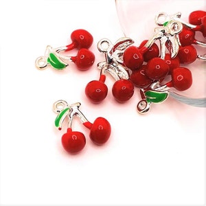 Puede incluir: Un grupo de colgantes de amuleto de plata con forma de cerezas. Las cerezas son rojas con hojas y tallos verdes. Los amuletos son perfectos para agregar un toque de fantasía a las joyas o las manualidades.