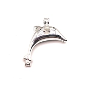 Op de afbeelding: Zilveren dolfijnvormige hanger met een ronde opening voor een parel of andere kleine bedel. De hanger heeft een scharnierende opening en een lus aan de bovenkant om aan een ketting te bevestigen.