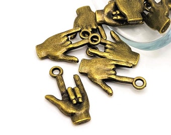 Puede incluir: Un grupo de abalorios de metal dorado antiguo en forma de manos haciendo el gesto de lenguaje de señas 'Te amo'. Cada abalorio tiene un pequeño anillo de salto para sujetarlo a joyas u otras manualidades.