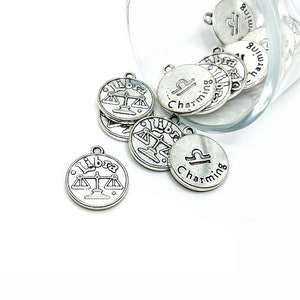 May include: Silver charm pendants with the zodiac sign Libra and the word "Charming" on them.